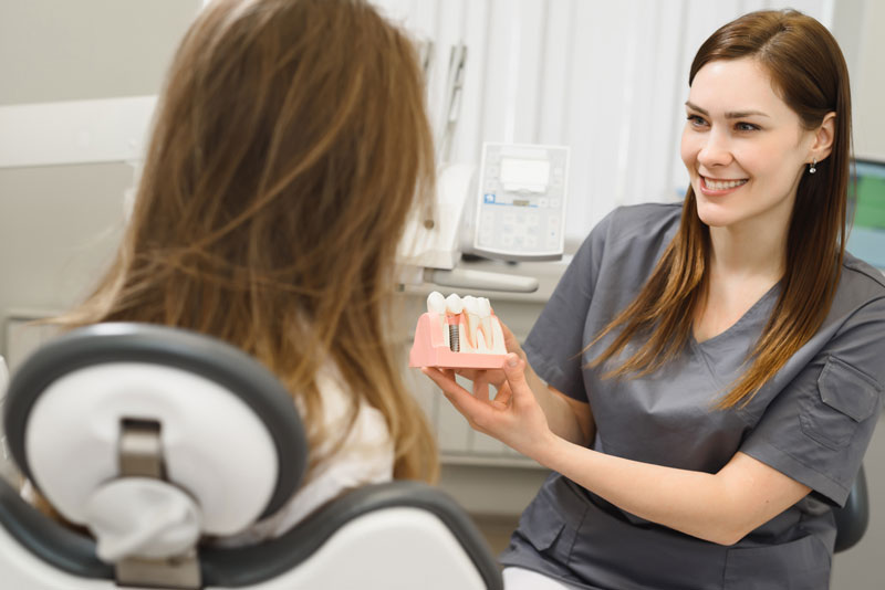 a picture of a dental assistant happily showing a dental implant candidate a dental implant model.