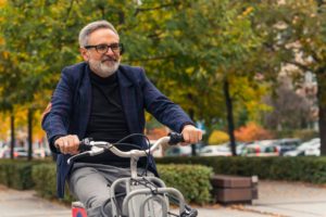 an older dental patient smiling and riding his bike after full mouth dental implant surgery.